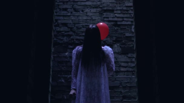 Безумная женщина в белом платье с красным шаром за спиной, атмосфера ужаса — стоковое видео