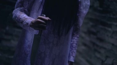 Önlüklü, elinde keskin bir bıçak, yüzü siyah saçlarla kaplı bir zombi gelin.