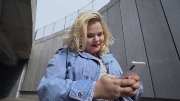 Симпатичная девушка с избыточным весом с помощью мессенджера приложение на гаджет, поколение z образ жизни — стоковое видео