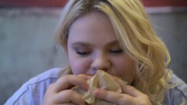 Fast food bağımlısı yağlı burger çiğneyen genç kadın stresten yeme bozukluğu yaşıyor.