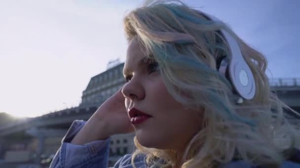 Красива жінка насолоджується улюбленою піснею в навушниках, захоплюючись заходом сонця у великому місті — стокове відео