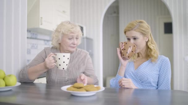 Młoda kobieta i matka rozmawiają, piją herbatę w kuchni, bliskie stosunki rodzinne — Wideo stockowe