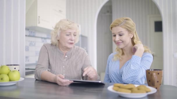 Mujer jubilada desplazándose imágenes en la tableta, madre e hija de compras en línea — Vídeo de stock