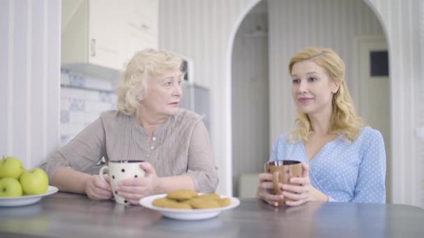 Femme âgée écoutant sa fille, parlant à la maison, tenant des tasses de thé, en famille — Video