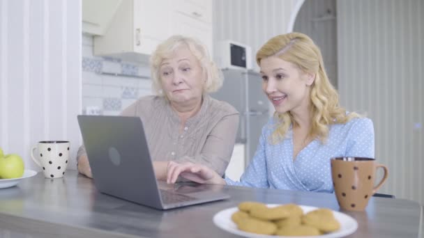 Ευτυχής μητέρα και η κόρη επιλέγουν ρούχα σε απευθείας σύνδεση, χρησιμοποιώντας την εφαρμογή αγορών στο laptop — Αρχείο Βίντεο