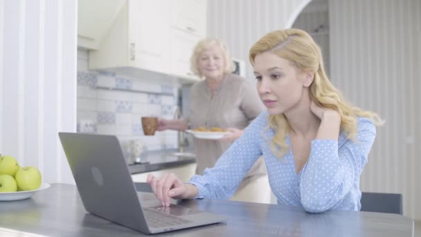 Matka opiekuje się córką, pracuje na laptopie, oferuje herbatę i ciasteczka — Wideo stockowe