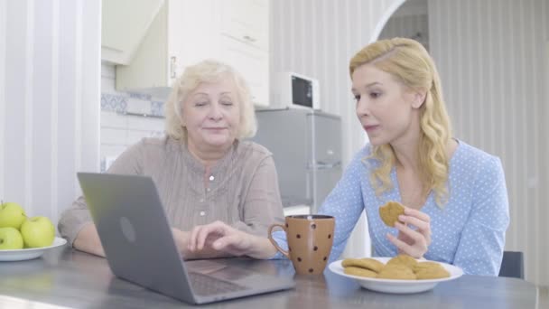 Mujer anciana y su hija viendo la película en el ordenador portátil en casa, beber té, ocio — Vídeo de stock