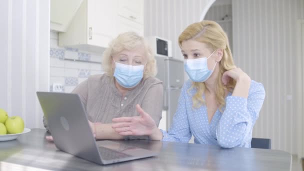 戴着防护面具的母亲和女儿在笔记本电脑、验尸机上阅读坏消息 — 图库视频影像
