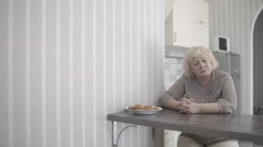 Çaresiz yaşlı kadın ailesini özlüyor, evde yalnız oturuyor, melankoli içinde yaşlanıyor.