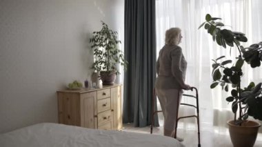 Pencere kenarında duran yaşlı bir kadın yürüyüş çerçevesiyle, huzurevinde terk edilmiş.