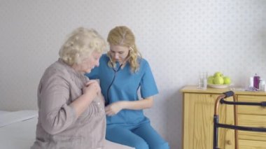 Genç kardiyolog evde hasta yaşlı bir kadını muayene ediyor, sağlık hizmetleri...