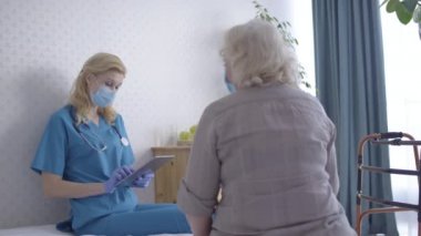 Doktor kıdemli hastayla konuşuyor, verileri tablete koyuyor, ev danışmanlığı yapıyor.