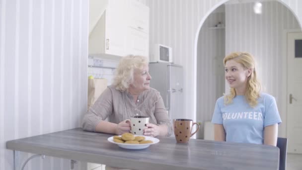 Amistosa señora mayor hablando con una joven voluntaria en un hogar de ancianos, cuidado — Vídeos de Stock
