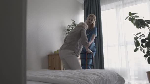 Miła młoda pielęgniarka pomaga niepełnosprawnej starszej pani używać ramki spacerowej, rehabilitacji — Wideo stockowe