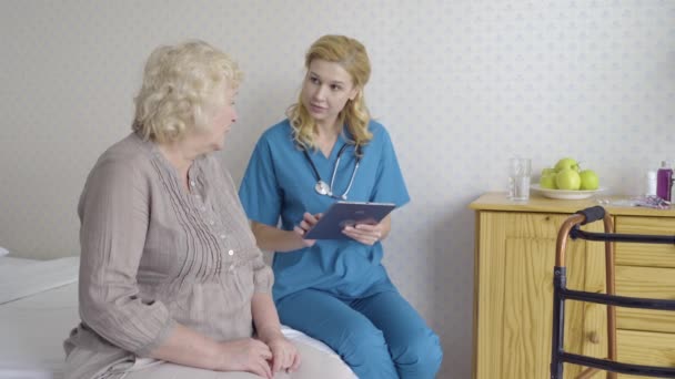 Médico hablando con paciente mayor insertando datos en pestaña, servicios médicos en casa — Vídeo de stock