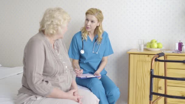 Γυναίκα γιατρός μιλάει σε ηλικιωμένους ασθενείς γράφοντας χαρτιά συνταγογράφησης, υγειονομική περίθαλψη — Αρχείο Βίντεο