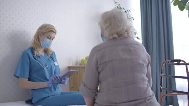 Lekarz rozmawiający ze starszym pacjentem, umieszczający dane w tabletkach, konsultacja domowa — Wideo stockowe