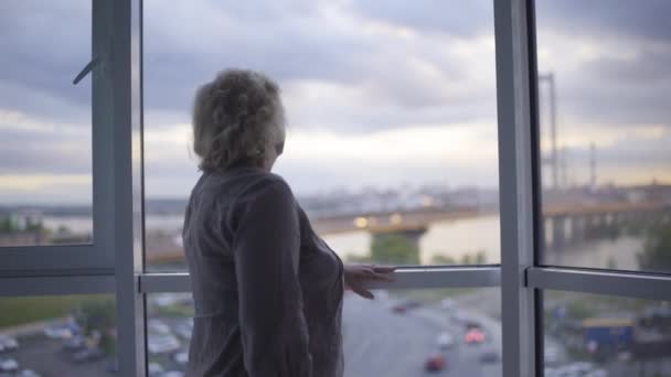 Високопоставлена жінка, що стоїть біля вікна, страждає самотністю в будинку престарілих — стокове відео