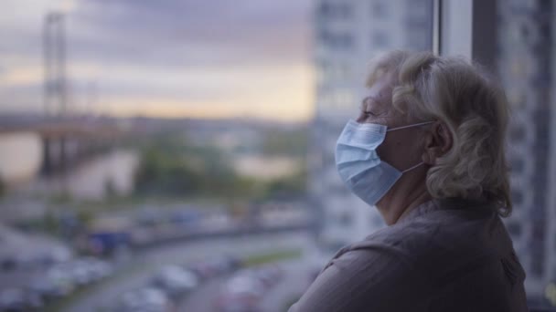 Infekterad gammal patient stående vid sjukhusfönster, klädd i skyddande ansiktsmask — Stockvideo