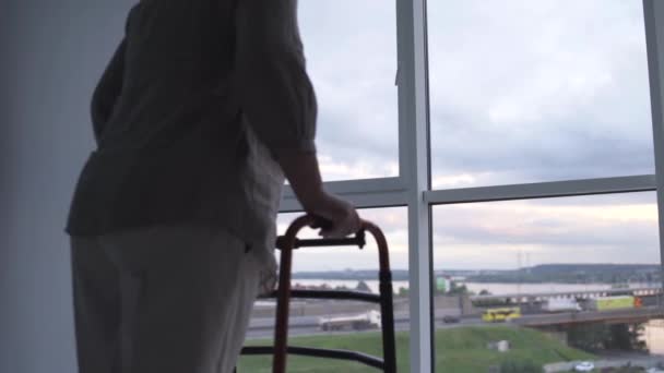 Désactive femme âgée approchant fenêtre avec marcheur, souffrant de solitude — Video