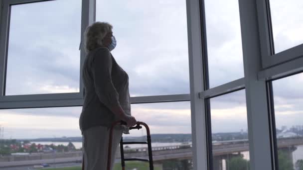 Malheureuse vieille femme malade en masque de protection, debout par la fenêtre, épidémie de grande ville — Video