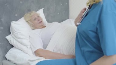 Hasta yaşlı kadın yatağında yatıyor genç doktorla konuşuyor, evde sağlık hizmetleri...
