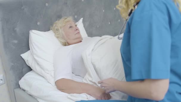 Enfermera cuidando a anciana enferma en la cama, servicios médicos en casa, caridad — Vídeos de Stock
