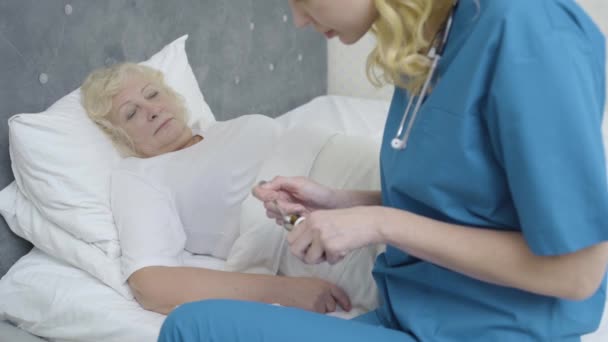 Enfermera ayudando a anciana enferma a tomar medicamentos, atención médica y apoyo en el hogar — Vídeo de stock