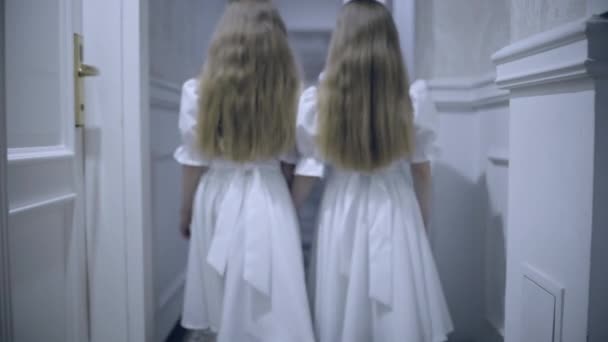 Little twin sisters slowly walking in empty hallway, haunted hotel atmosphere — Stock Video