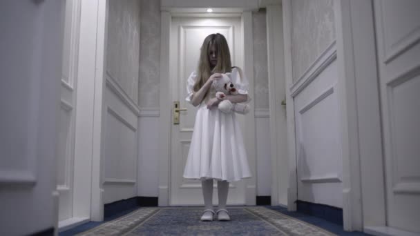 Страшный ребенок-призрак, ласкающий кровавого игрушечного медведя, стоящего в коридоре в одиночестве, кошмар — стоковое видео