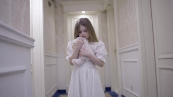 Расстроенная маленькая сиротка обнимает игрушку, ходит одна в большом доме, усыновляет ребенка — стоковое видео