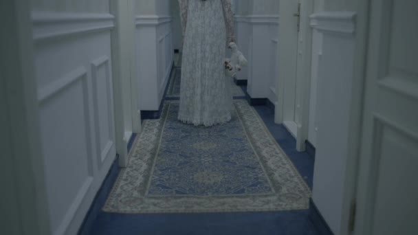 Безумная женщина в свадебном платье с игрушкой, идущая по коридору, вид сзади, психопатка — стоковое видео