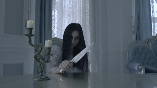 Brunett kvinna håller kniv i handen, sitter vid bordet, innehav av djävulen — Stockvideo