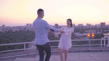 Mutlu çift el ele tutuşuyor, çatıda buluşuyorlar, romantik şehir manzarası var.