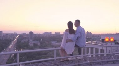 Çatıda oturmuş büyük şehir ışıklarına hayran olan genç bir çiftin romantik randevusu.