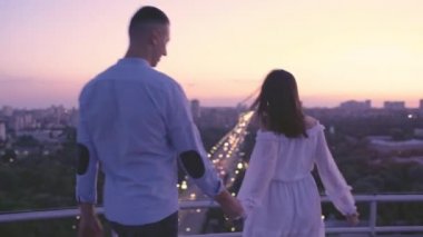 Romantik kız arkadaş genç adamın elini tutuyor, çift şehir manzarasından birlikte zevk alıyor.