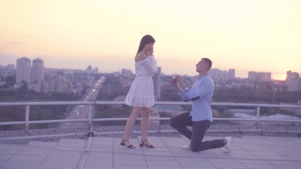 Молодий чоловік на колінах робить пропозицію дівчині на даху, романтична пара — стокове відео