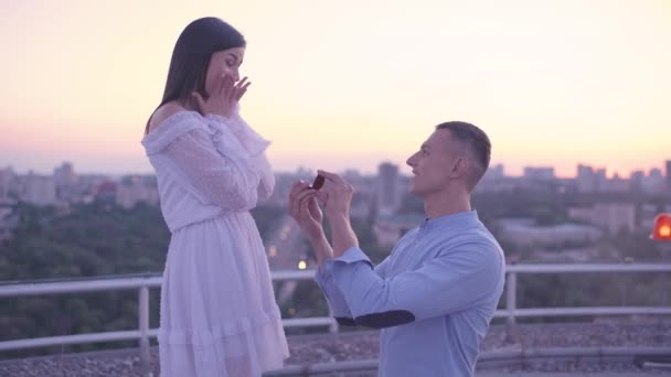 Захоплена дівчина приймає обручку від хлопця, романтична пропозиція на даху — стокове відео