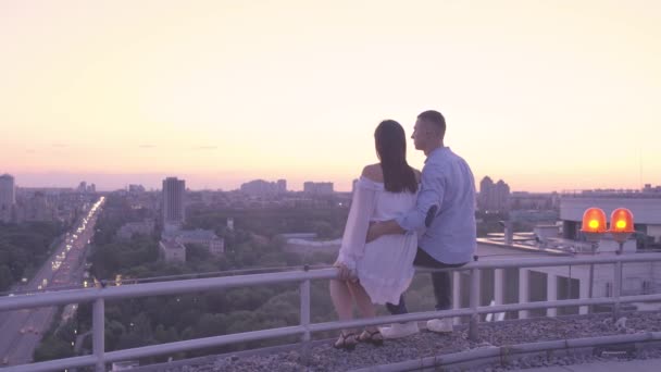 Romantische datum van jonge liefde paar zitten op het dak, het bewonderen van grote stad lichten — Stockvideo