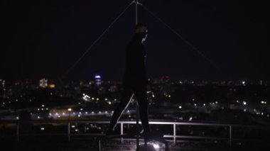 Siyah kıyafetli maskeli adam gece çatıda duruyor, gizli bir operasyon.