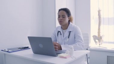 Gülümseyen doktor internette hastaya danışmanlık yapıyor, dizüstü bilgisayar uygulaması kullanıyor, teşhis koyuyor.