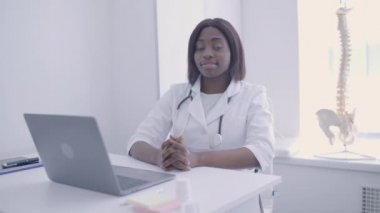 Kameraya gülümseyen, ofiste masada oturan nitelikli kadın terapist.