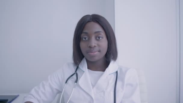 Steteskoplu Afro-Amerikalı doktor kameraya, tıbbi personele, kliniğe bakıyor. — Stok video