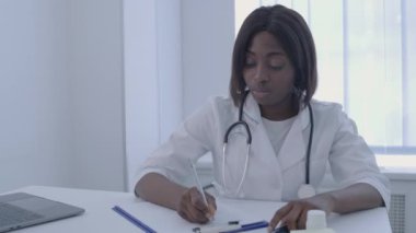 Afro-Amerikalı terapist ofiste evrakları dolduruyor, tıbbi geçmiş yazıyor.