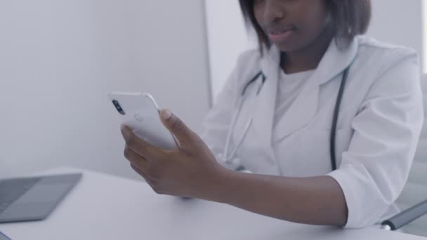Африканская женщина-врач читает медицинские записи онлайн, прокручивает телефон, устройство — стоковое видео
