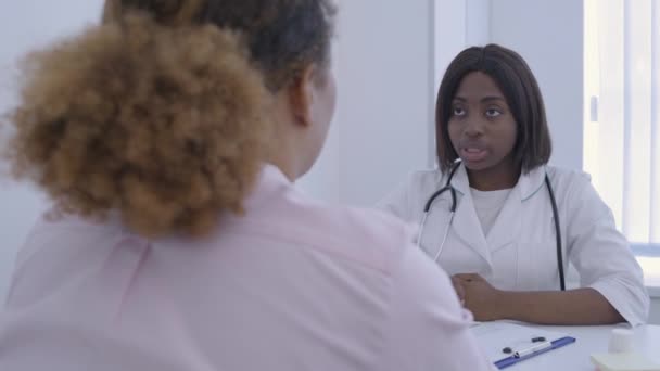 Afrikansk kvinnlig läkare talar med patienten på kliniken, diskuterar symtom, hälsa — Stockvideo