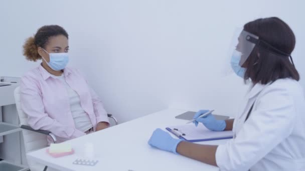 Arzt in Maske fragt Patient nach Symptomen, schreibt in Dokument — Stockvideo