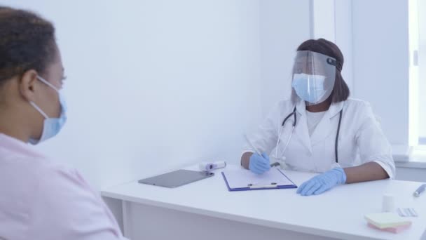Θηλυκός ιατρός σε προστατευτική ασπίδα προσώπου που ελέγχει τη θερμοκρασία του ασθενούς, ιός — Αρχείο Βίντεο
