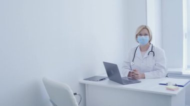 Maskeli doktor masada oturuyor, fiziksel muayene, hastanede kontrol.