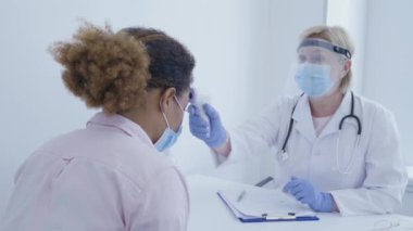 Doktor, kızılötesi termometre ve covid 19 salgınıyla hasta sıcaklığını ölçüyor.